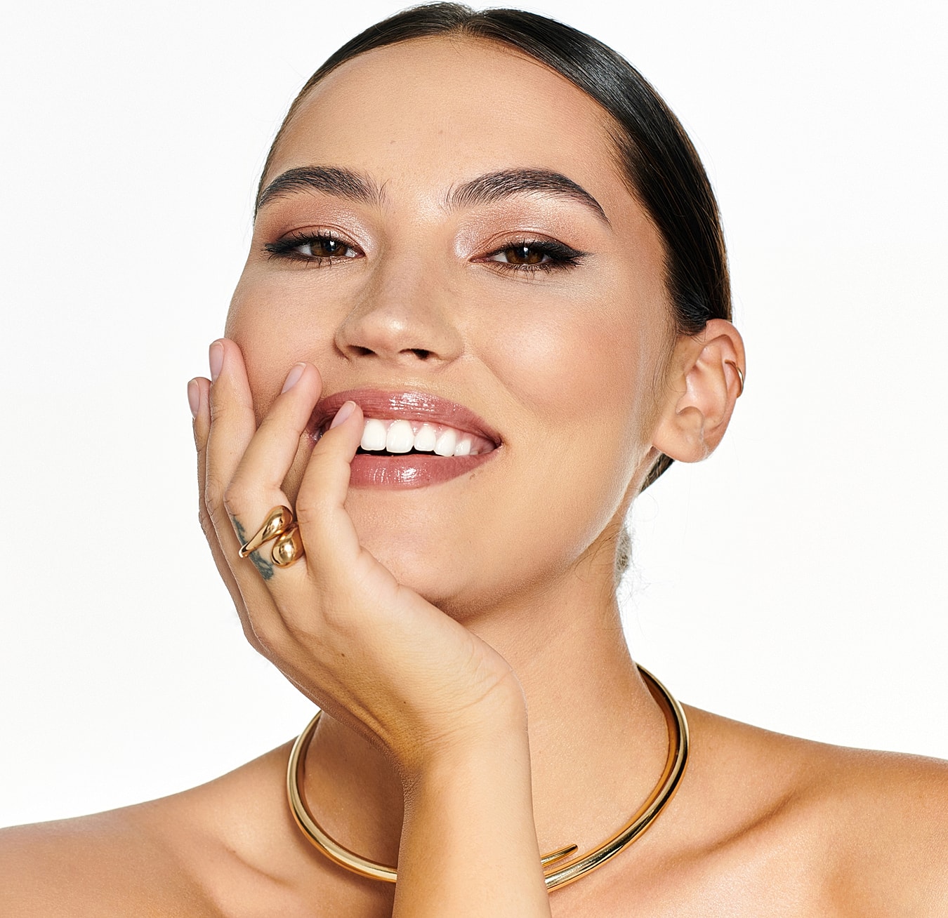 Smiling woman showcasing jewelry with natural makeup.