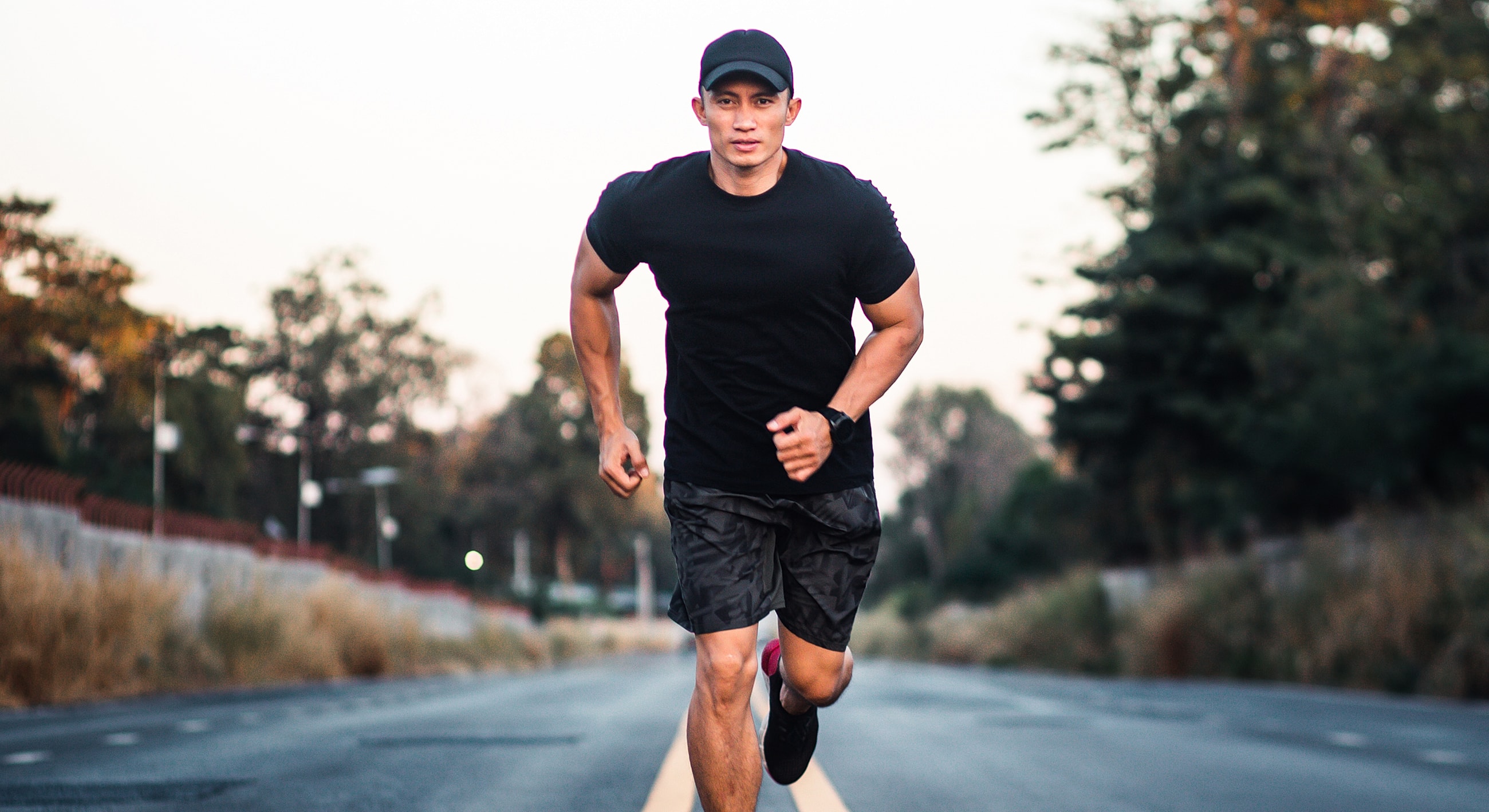 Runner in black attire on empty road.